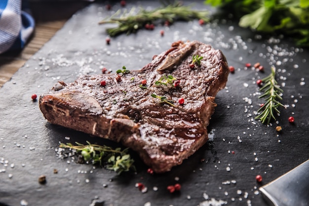 Stek wołowy T-Bone z solą, pieprzem i rozmarynem na łupkowym talerzu.