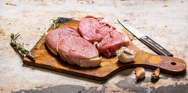Stek ze świeżego surowego mięsa z przyprawami na drewnianej desce. Na tle rustykalnym.
