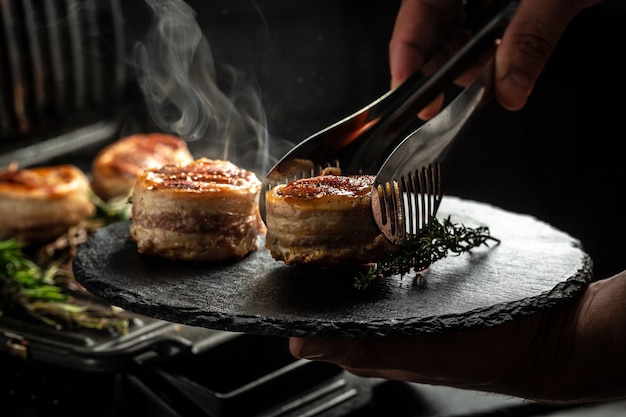 Steki medaliony z polędwicy wołowej pokryte boczkiem na grillu z ciemnym dymnym tłem. Gotowanie stek wołowy na grillu przez ręce szefa kuchni.