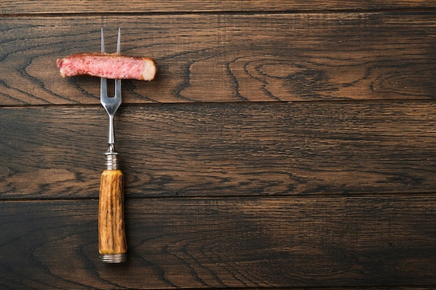 Zdjęcie steki tbone plasterki wołowiny grillowany stek z grilla mięsnego na widelcu do mięsa na spalonym ciemnym drewnianym tle z miejscem na kopię tekstu widok z góry makieta