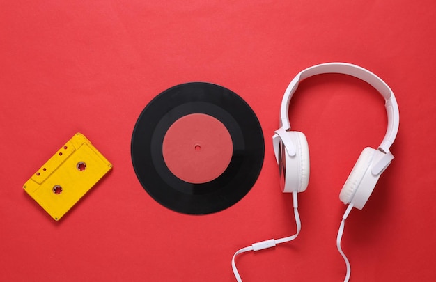 Stereofoniczne słuchawki z płytą winylową na kasecie audio na czerwonym tle Martwa natura w stylu retro z lat 80. Widok z góry