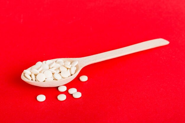 Sterta białych tabletek na kolorowym tle Tabletki rozrzucone na stole Kupie czerwone miękkie kapsułki żelatynowe Koncepcja witamin i suplementów diety