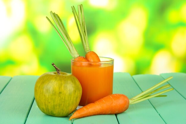 Zdjęcie sterta marchwi i szklanka soku z zielonego jabłka na kolorowym drewnianym stole na jasnym tle
