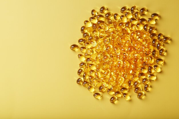 Sterta przezroczystych kapsułek oleju rybnego na żółtym tle z wolną przestrzenią