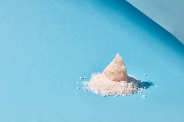Sterty soli morskiej mineralnych i duży kryształ na białym tle na niebieskim tle z miejsca kopiowania.