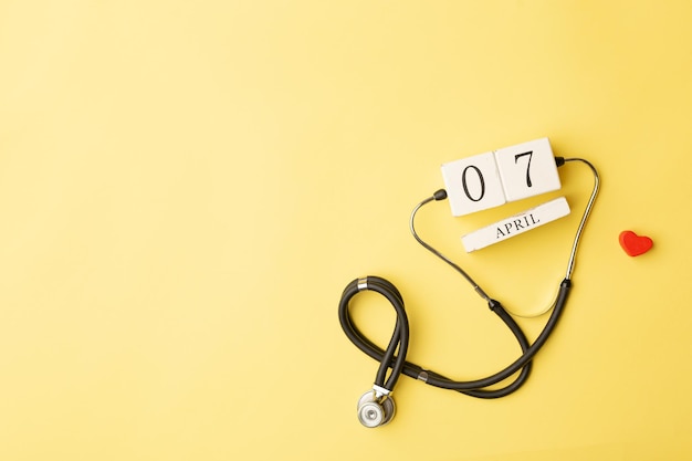 Stetoskop czerwone serce i kalendarz 7 kwietnia na żółtym tle z kopią miejsca na tekst