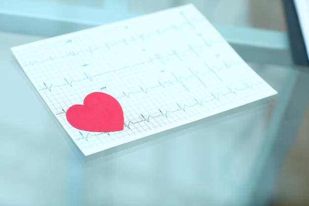Zdjęcie stetoskop kardiogram i czerwone papierowe serce na stole