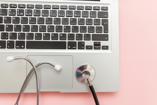 Stetoskop klawiatury laptopa na białym tle na różowym tle. Nowoczesna medyczna koncepcja technologii informacyjnej i oprogramowania. Diagnostyka i naprawa komputerów i gadżetów. Płaski widok z góry