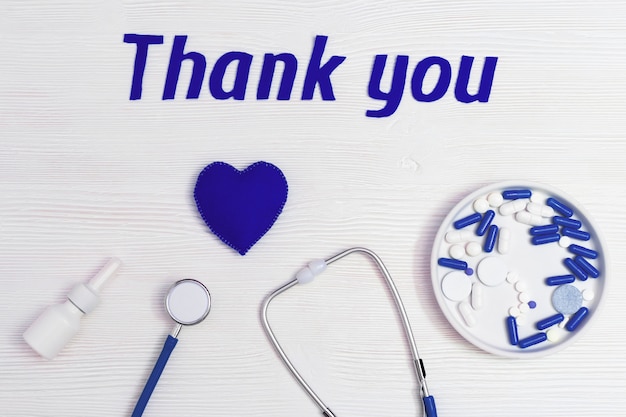Stetoskop, niebieskie serce, aerozol do nosa, pigułki i tekst „dziękuję” na białej drewnianej powierzchni
