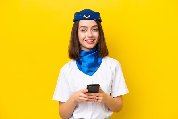 Stewardesa samolotu Ukrainka na białym tle na żółtym tle wysyłająca wiadomość za pomocą telefonu komórkowego