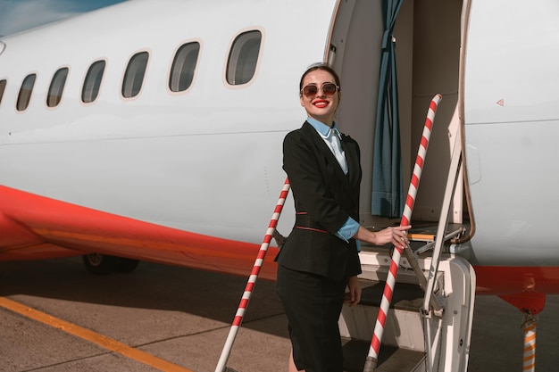 Stewardesa w okularach przeciwsłonecznych stojąca na schodach samolotu na lotnisku i odwracająca wzrok