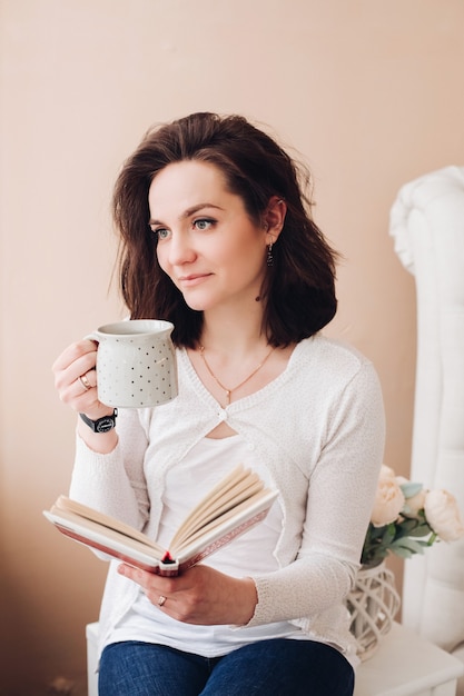 Stock photo portret atrakcyjnej młodej kobiety rasy kaukaskiej z książką picia kawy odwracając zamyślony.