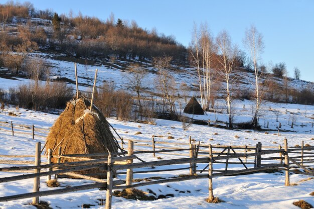 Stogi siana i ogrodzenie z drewna, zimowy krajobraz, życie na wsi, odpoczynek w górach we wsi