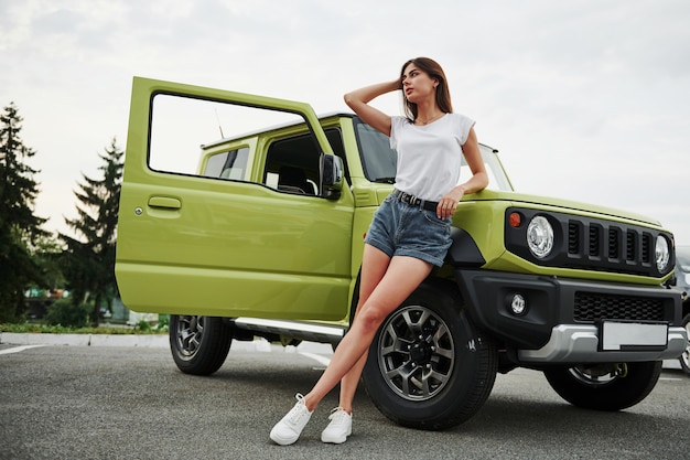Zdjęcie stoi w pobliżu nowego pojazdu. ładna kobieta w zielonym nowoczesnym samochodzie pozuje do aparatu.
