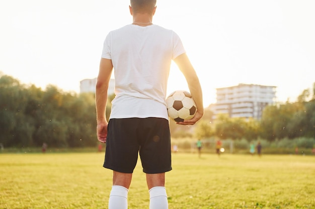 Stojąc i trzymając piłkę w ręku Młody piłkarz trenuje na boisku sportowym