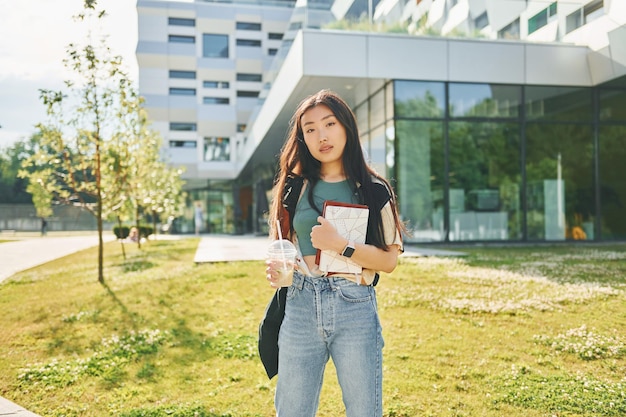Stojąc na tle nowoczesnego budynku Młoda azjatycka kobieta jest na zewnątrz w ciągu dnia