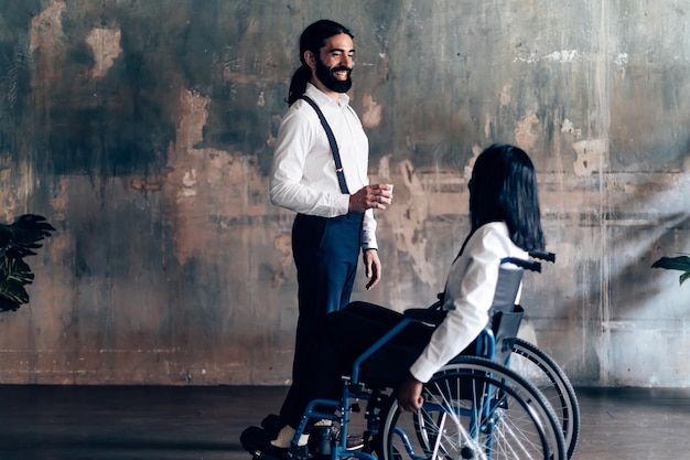 Stojący elegancki dżentelmen rozmawiający z kobietą na wózku inwalidzkim dwóch kolegów z różnych grup etnicznych rozmawiających razem podczas przerwy w pracy