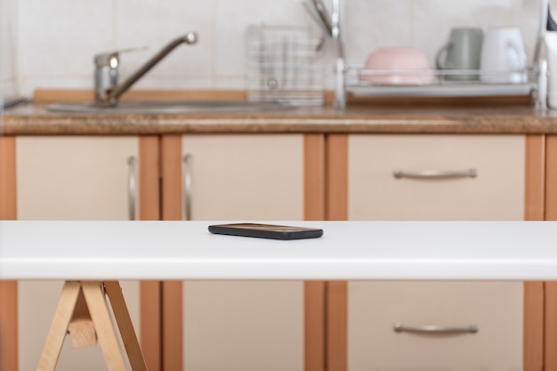 Zdjęcie stół kuchenny i telefon komórkowy na tle kuchni. zapomniany smartfon