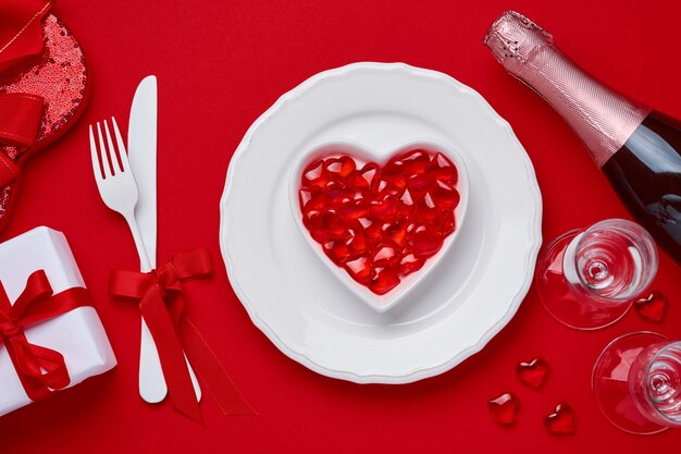 Stół lub koncepcja Walentynki z pustym białym talerzem i sztućcami, widelcem i nożem, szampanem, kieliszkami i pudełkiem na szkarłatny lub czerwony stół. Widok z góry na płasko leżał z miejscem na kopię.
