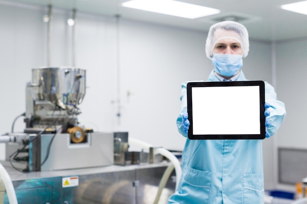 Stół na ostrości blured tle Pracownik fabryki stoi w pobliżu maszyny i pokazuje pustą tabletkę