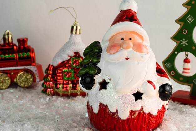 Stół pokryty płatkami śniegu z dekoracjami świątecznymi. Święty Mikołaj, choinka z czerwonymi, złotymi kulkami i światłami. Selektywne skupienie.