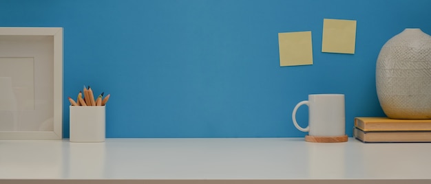 Stół roboczy z papeterią i dekoracjami na białym biurku z niebieską ścianą
