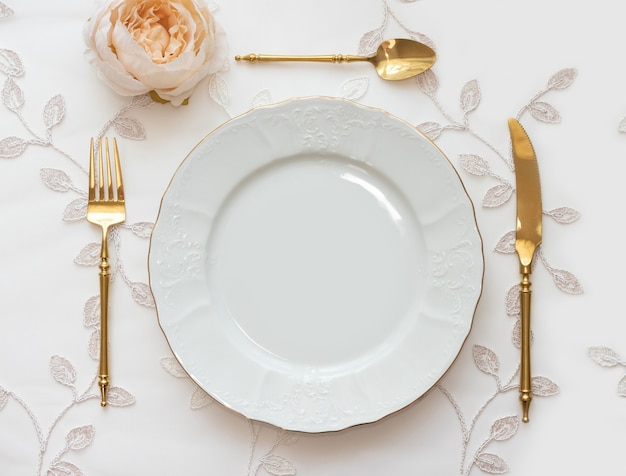 Stół weselny zaaranżowany ze złotymi sztućcami i białą ładowarką