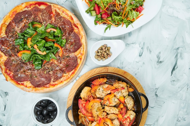 Stół z dużą ilością jedzenia na lunch, zdrową sałatką, pizzą z cielęciną vitello tonatto i patelnią z kurczaka z pomidorami. Stół rozkładany na płasko