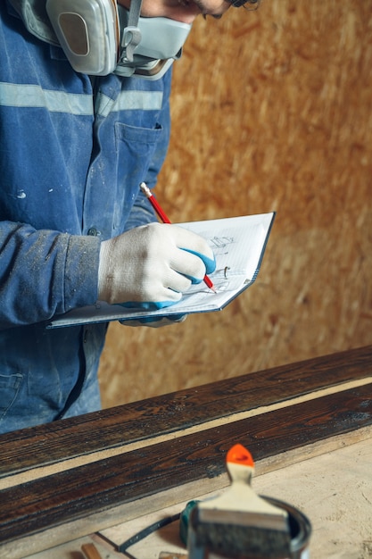 Zdjęcie stolarz człowiek w swoim domowym studio pracuje z drewnem i rysuje szkice ołówkiem w zeszycie