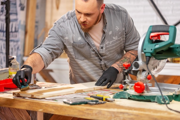 Stolarz pokrywa lakierem drewniany przedmiot w warsztacie