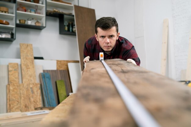 Stolarz w pracy mężczyzna mierzy i zaznacza drewnianą deskę za pomocą metalowej linijki i ołówka