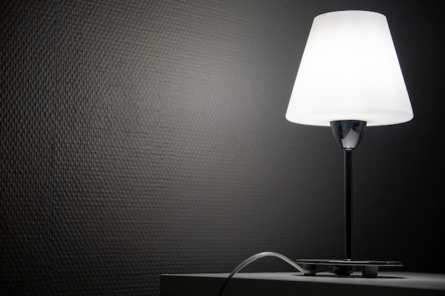 Stolik nocny i płonąca lampa stoją na nim w ciemnym pokoju Numer hotelu