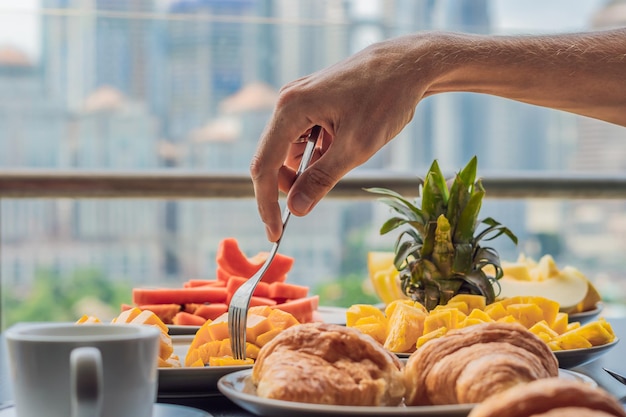 Stolik śniadaniowy z owocami kawy i rogalikiem chlebowym na balkonie na tle dużego