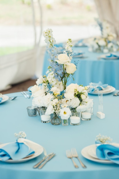 Stoły weselne dla gości okrągłe stoły z niebieskim obrusem ozdobione kwiatami talerze kieliszki...