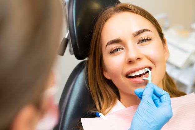 Stomatolog pokazuje młodej kobiecie w gabinecie dentystycznym, jak używać nici dentystycznej