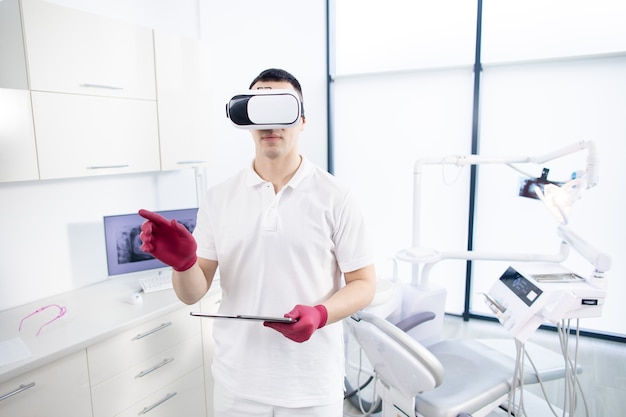 Zdjęcie stomatolog w mundurze stoi w gabinecie i sprawdza cyfrowy obraz przed wizytą pacjenta.