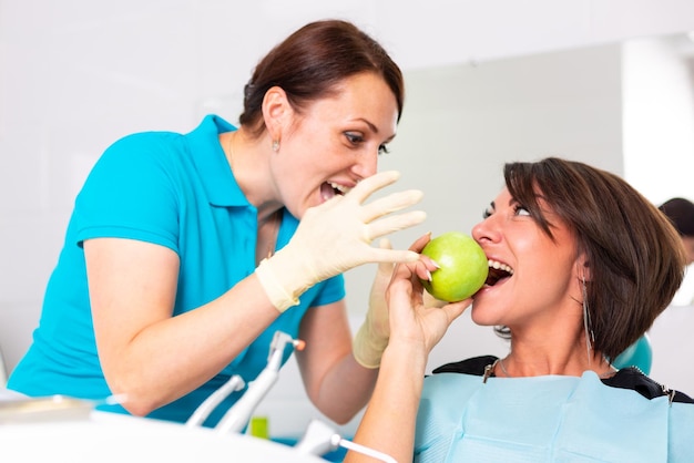 Stomatologia zdrowe zęby Dentysta podaje zielone jabłko pięknej dziewczynie pacjentce w celu sprawdzenia zębów Badanie zębów zielonym jabłkiem
