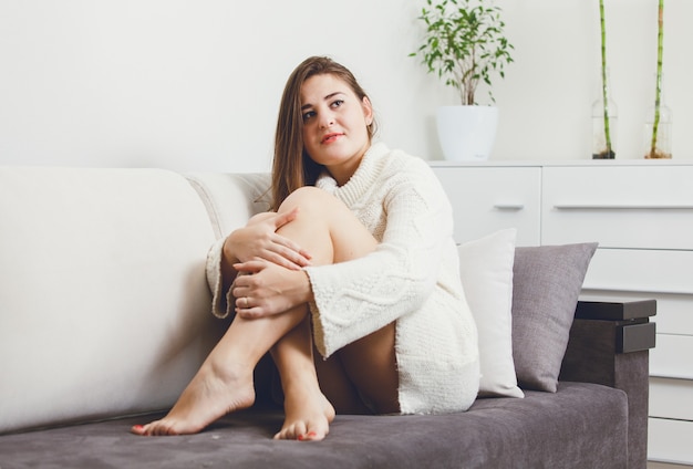 Stonowany portret brunetki kobiety siedzącej na kanapie w swetrze