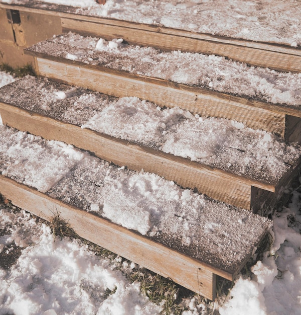 Stopnie drewnianych schodów pokryte są śniegiem podczas opadów śniegu Zejście na podwórko domu Zimny dzień we wsi