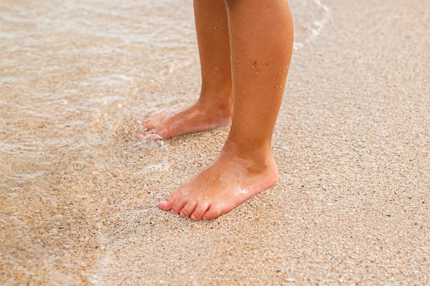 Stopy dzieci stoją blisko morza na piaszczystej plaży.