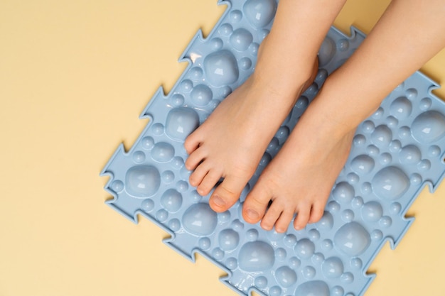 Stopy dziecięce na niebieskim dywaniku ortopedycznym na beżowym tle leczenie i profilaktyka płaskostopia palucha koślawego