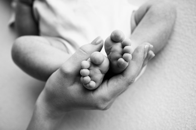 Stopy dziecka w rękach matki ojca starszego brata lub siostry rodziny Stopy malutkiego noworodka z bliska Stopy małych dzieci otoczone dłońmi rodziny Czarno-białe