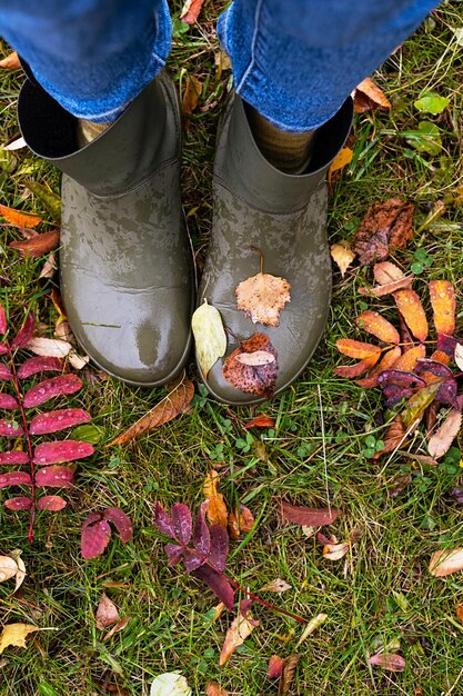 Zdjęcie stopy w gumowych butach stojących w mokrej trawie z kolorowymi opadłymi liśćmi koncepcja jesiennego stylu życia