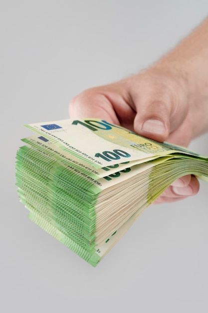 Stos banknotów euro w ręku Duży stos banknotów 100 euro w męskiej dłoni na jednolitym szarym tle Pojęcie pomocy finansowej zakup nieruchomości płatność pożyczka lub ubezpieczenie