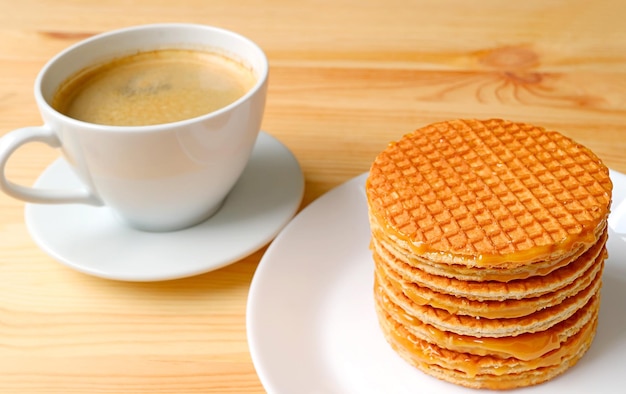 Stos holenderskich stroopwafelów na białym talerzu z rozmazaną gorącą kawą w tle