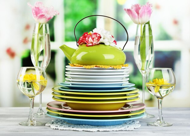 Stos kolorowych naczyń ceramicznych i kwiatów na drewnianym stole na jasnym tle