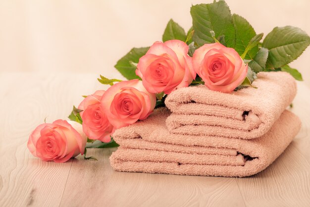 Stos miękkich ręczników frotte z czerwonymi różami w różowym tle.