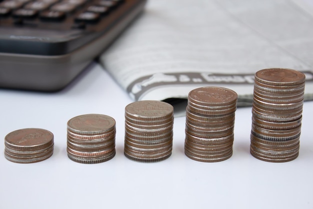 Stos monet na stole z kalkulatorem i gazetą Zarządzanie pieniędzmi koncepcja oszczędności i inwestycji