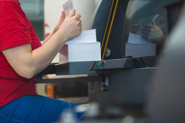 Stos papieru w rękach pracownic przed maszyną drukarską