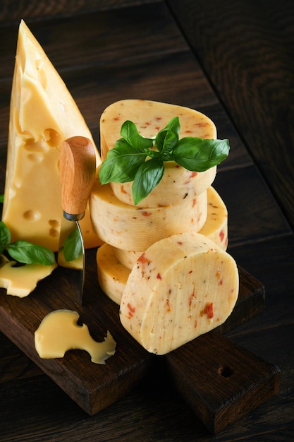 Zdjęcie stos sera z pomidorami i przyprawami i serem szwajcarskim z bazylią i nożem na desce do serwowania na ciemnym tle drewnianego stołu asortyment różnych rodzajów sera tło sera